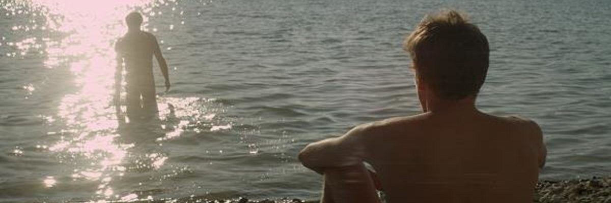 Widok na mężczyznę siedzący tyłem nad morzem podczas zachodu słońca, patrzący się na człowieka będącego w wodzie