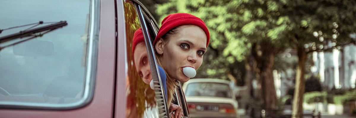 Kobieta w czerwonej czapce, robiąca balon z gumy, wyglądająca przez okno w samochodzie 
