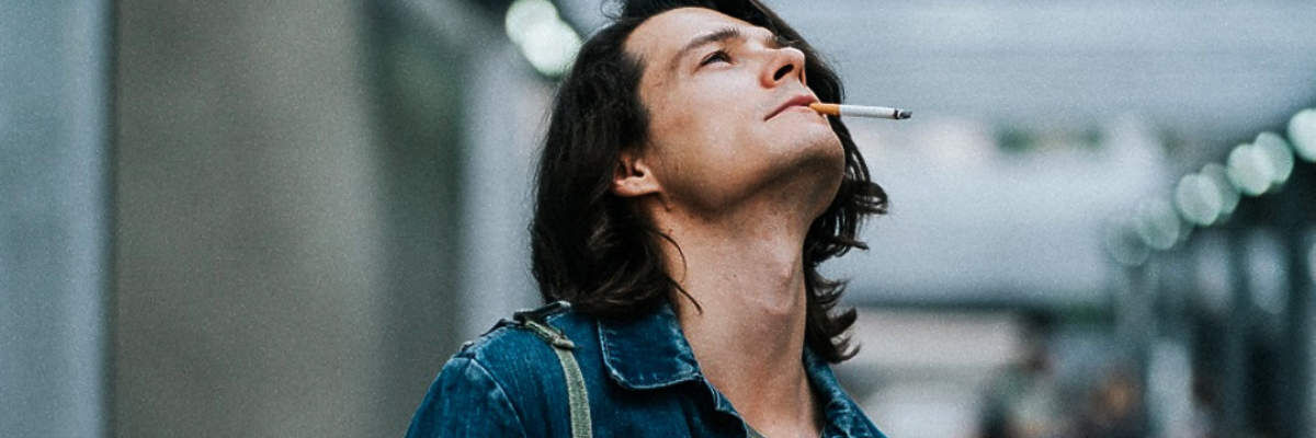 Młody mężczyzna z długimi włosami i papierosem w ustach