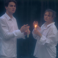 Mężczyzna i kobieta w białych koszulach stoją w rzece i trzymają palące się świece w dłoniach 