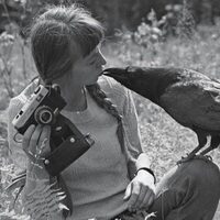 Czarno-białe zdjęcie Simony Kossak siedzącej na łonie natury i całującej ptaka siedzącego na jej kolanie 