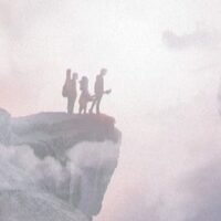 Czwórka ludzi stojących na skale na przeciwko drugiej skały unoszącej się w chmurach