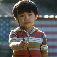 Azjatycki chłopiec niosący patyk. W tle flaga amerykańska na budynku
