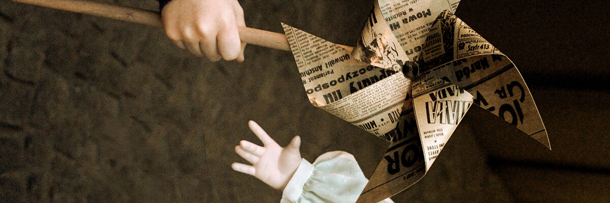 Dwie dłonie kukiełek, większa z nich trzyma wiatrak zrobiony z gazety 
