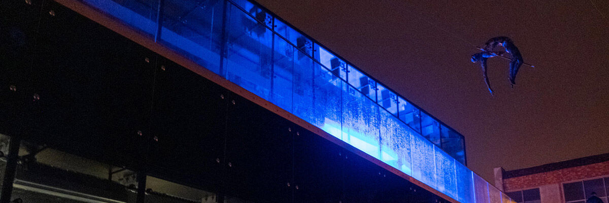 Balansująca rzeźba na tle nocnego nieba i oświetlony na niebiesko nowy budynek kawiarni na Starym Mieście 