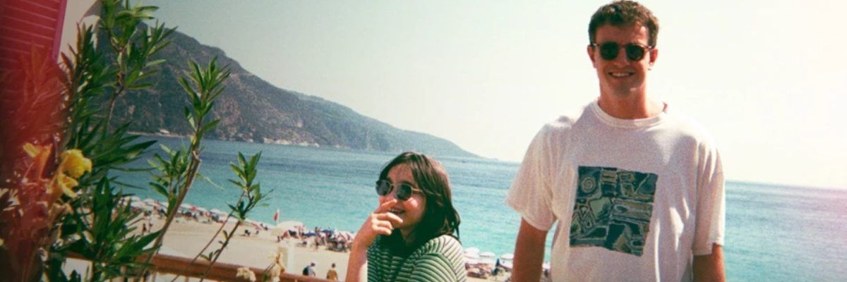 Chłopak stojący w koszulce z krótkim rękawkiem w okularach przeciwsłonecznych obok dziewczyny w okularach przeciwsłonecznych na tle morza