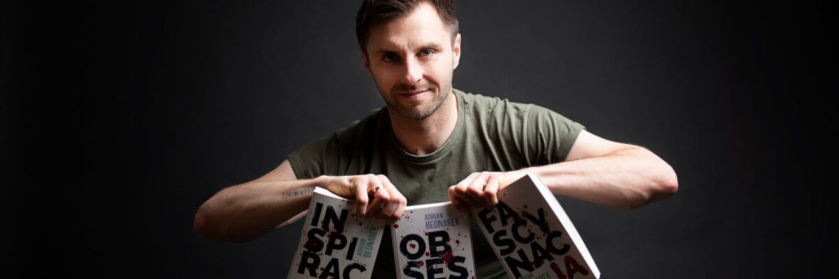 Pisarz Adrian Bedarek trzymający w dłoniach trzy egzemplarze swojej książki 