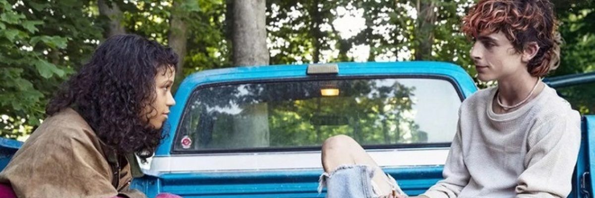 Dziewczyna siedząca na tyle niebieskiego samochodu, patrząca się na chłopaka siedzącego na przeciwko niej, też na tyle samochodu