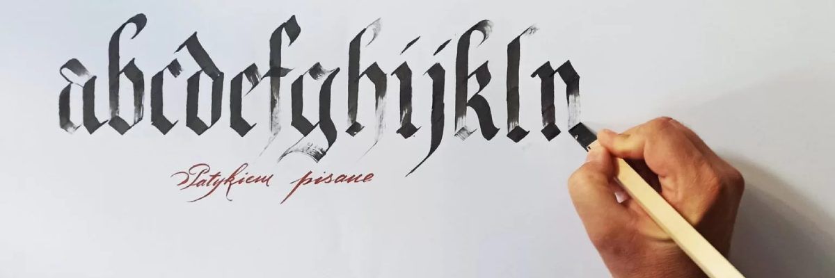 Pięknie napisane odręcznie litery "acdefghijklm", a po prawej stronie dłoń trzymająca pędzel. Niżej czerwony napis "patykiem pisane"