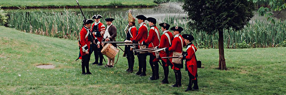 Mężczyźni ubrani w tradycyjne stroje  XVIII-wiecznej armii garnizonu jasnogórskiego tj. czerwony mundur i czarne spodnie oraz kapelusz