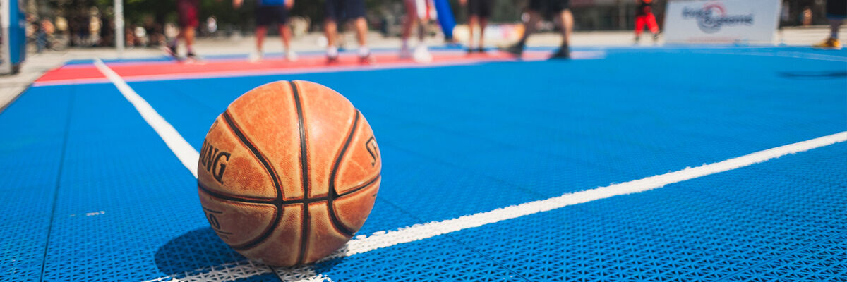 Pomarańczowa piłka do koszykówki leżąca na niebieskim korcie do koszykówki