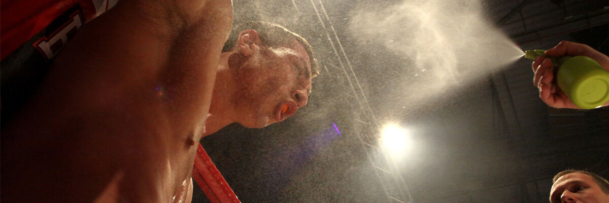 Mężczyzna opierający się o ring boxerski, spryskiwany wodą przez drugą osobę