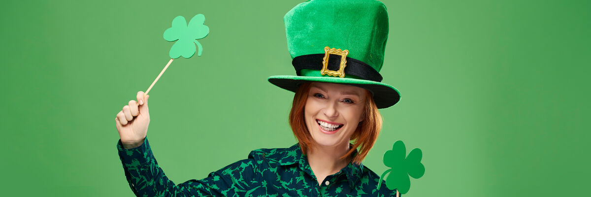 Uśmiechnięta kobieta w zielonym kapeluszu, trzymająca patyk, na którym jest przymocowany symbol czterolistnej koniczyny