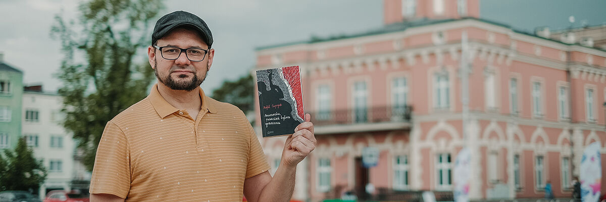 Pisarz Rafał Cuprjak trzymający w ręce swoją powieść na tle częstochowskiego ratusza
