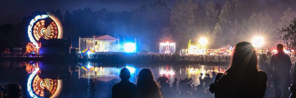 Fotografia Parku Lisiniec nocą podczas koncertu, podświetlona scena, świecące "diabelskie koło", publicznosć, zalew