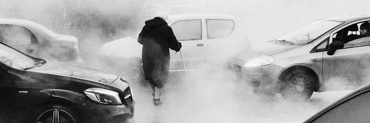 Starsza kobieta w dymie przechodząca przez ulicę między samochodami 